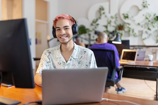 Gen_Z_worker Photo of a young office worker. He has pink hair and is wearing headphones.