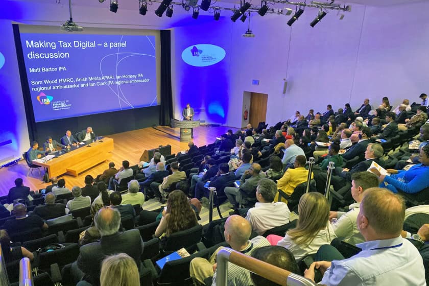 people at a conference, the room is lit with bright purple lights. They are all listening to an IFA presentation