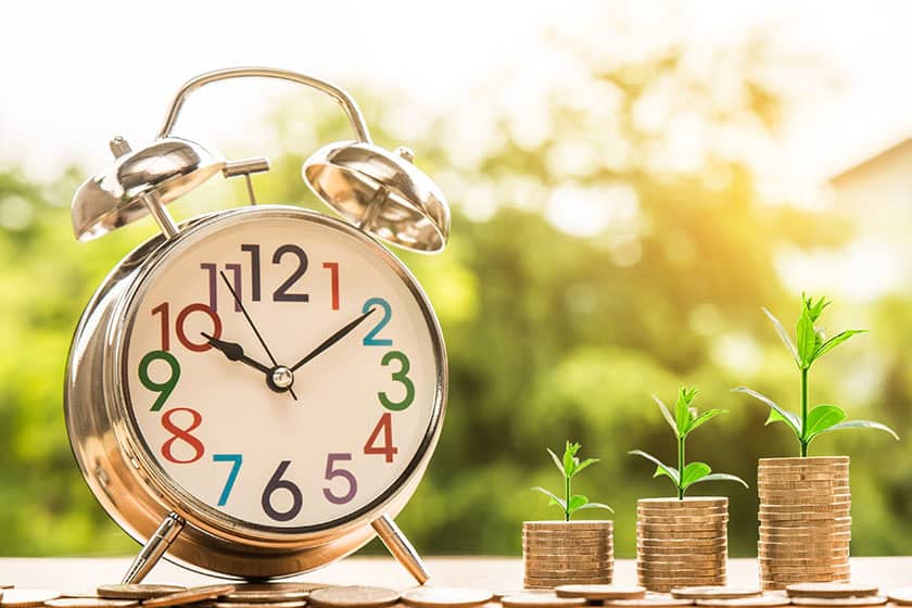 An alarm clock next to three neat piles of cins, each with a small seedling growing from the top.