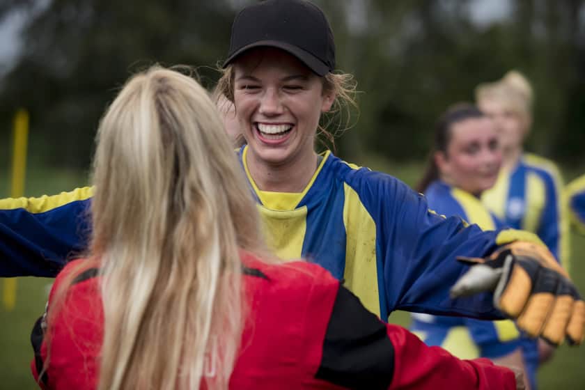 Women celebrating football victory. One of them is wearing a jersey and the other one is wearing normal clothes. The tone is victorious and filled with smiles.