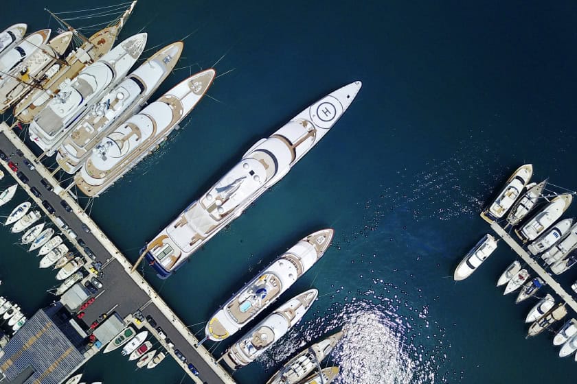 dockyard Photo of a yacht club. The photo is taken from the sky and it shows super yachts lined up next to one another.