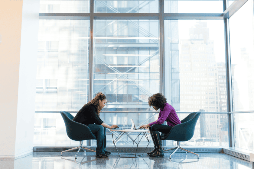 Two women seated beside each other staring at their laptops in deep thought