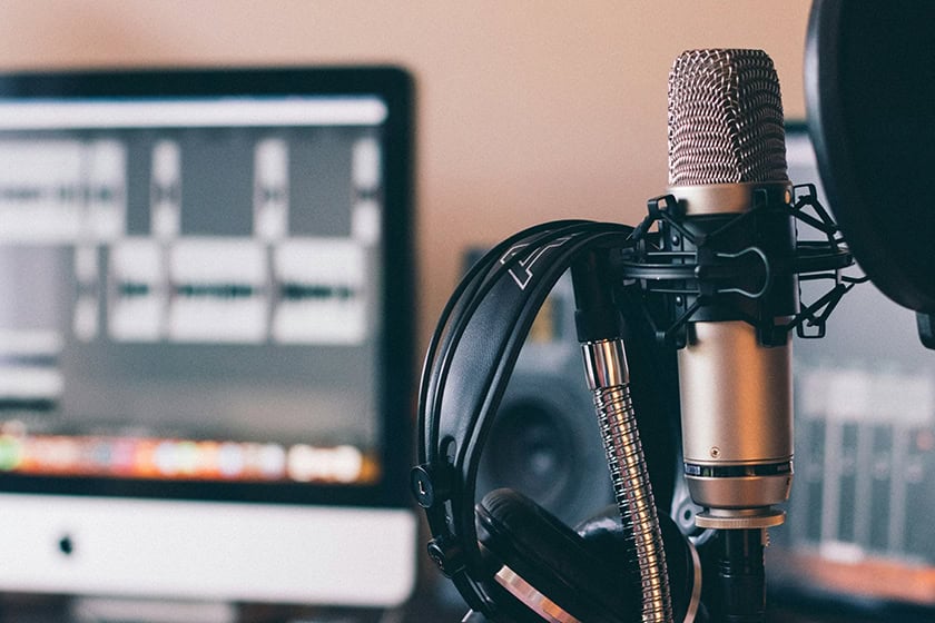 Microphone and headphones in front of a computer screen. Set up for recording a podcast.