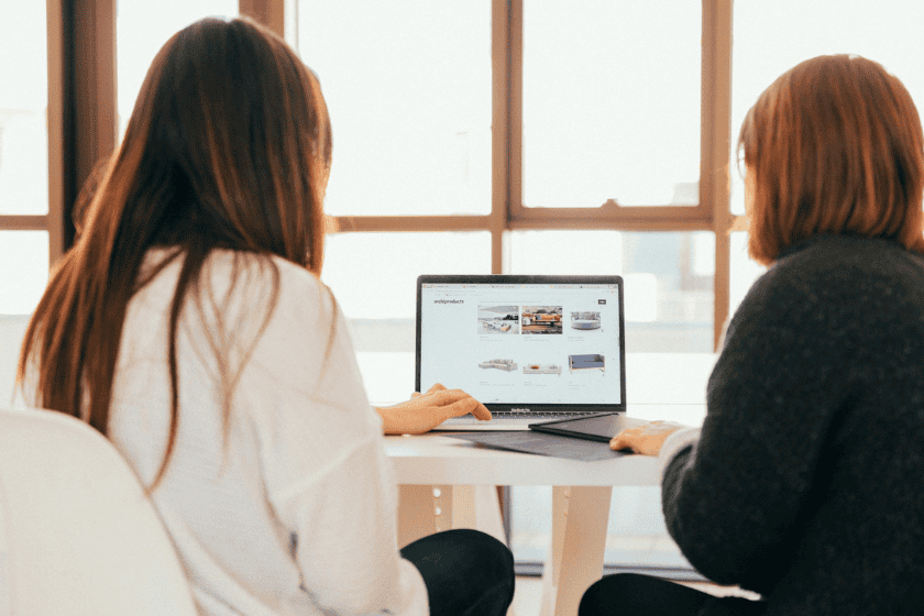 Two people seated at a table looking at a laptop screen together