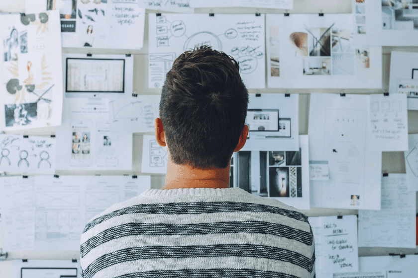 A man looks up at a wall filled with brainstorming notes and plans